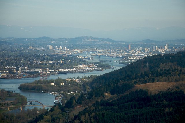 A broad river winding through a rather developed area, a city in the background, hills in both foreground and background