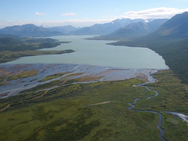 a lake among rugged mountains with a flat wetland area in the foreground, greenish terrain but without trees