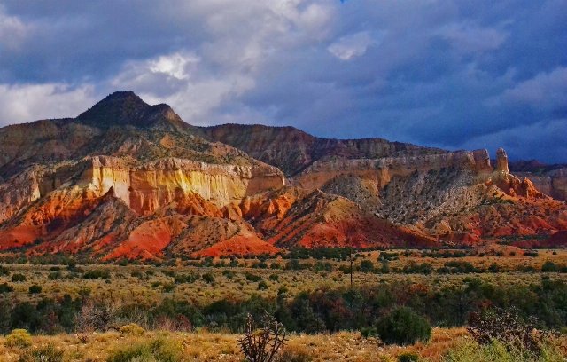 low, dry grass and stunted shrubs in a flat foreground, with dramatic red slopes rising to a rugged plateau behind