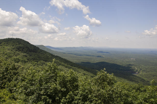 A forested, round-topped mountain on the left, with forested, mountainous terrain in the background.