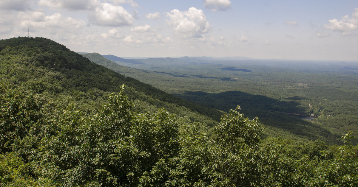 A forested, round-topped mountain on the left, with forested, mountainous terrain in the background.