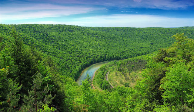 A small river winding through a landscape of low mountains covered in lush, green forests.