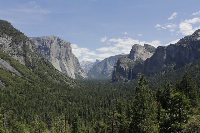 A dramatic mountain pass with barren, steep cliffs on both sides and a broad conifer-filled valley below