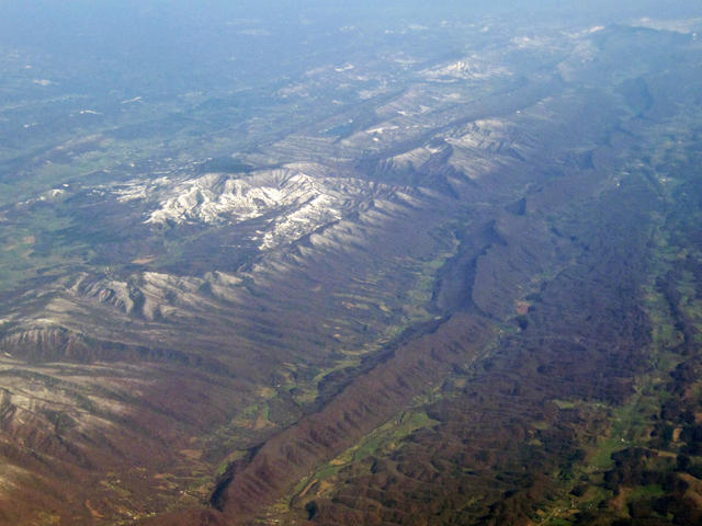 Aerial photo showing a long, unbroken ridge, some low valleys, and low snowy mountains, all oriented in long lines.