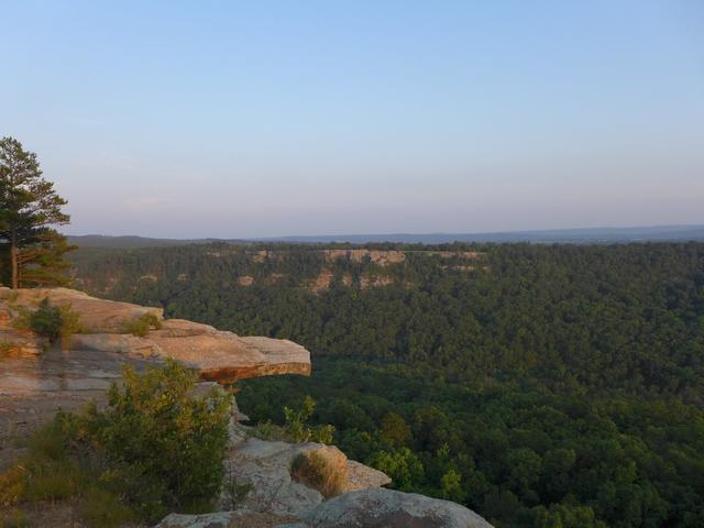 A rock outcropping with a long ridge and steep cliffs in the distance, extensive deciduous forest between.