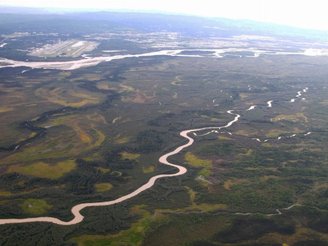 aerial photo showing a large river with many islands and a smaller river, with forests, wetlands, and a city in the distance