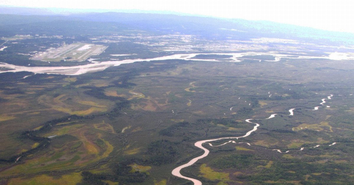 aerial photo showing a large river with many islands and a smaller river, with forests, wetlands, and a city in the distance