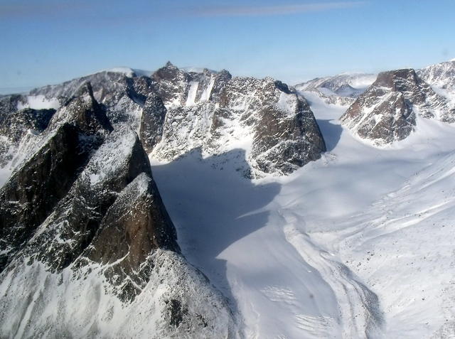 Steep mountain peaks dusted in snow, with a snow-covered glacier covering the rest of the landscape, under clear blue skies