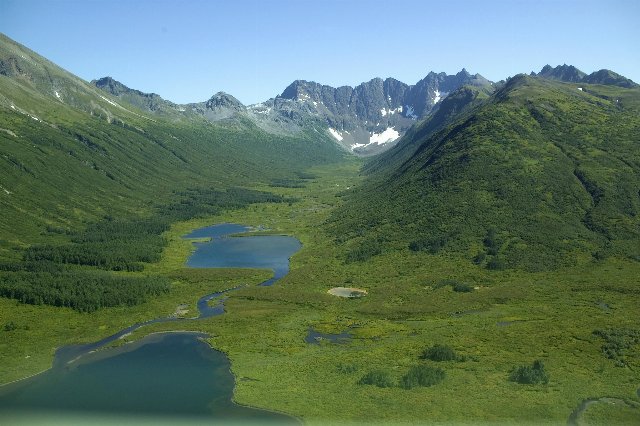 broad mountain valley with two lakes, forested slopes and steep, barren mountain caps with some snow