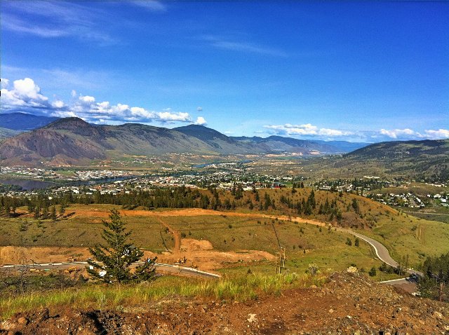 A valley with grassland and scattered trees, and a relatively low-density city, among hills and under a deep blue sky